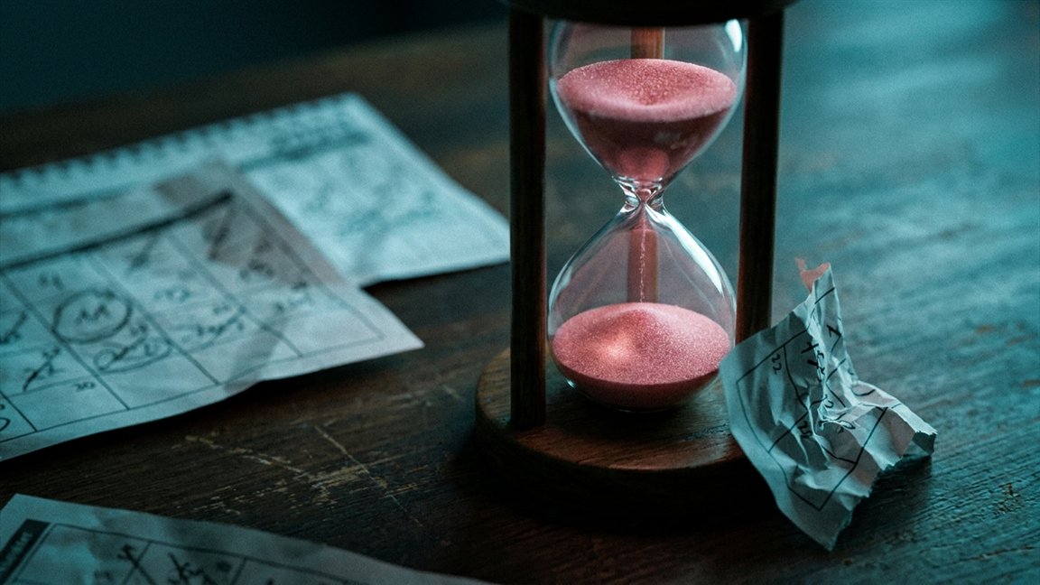 Reloj de arena con arena rosa entre páginas de calendario